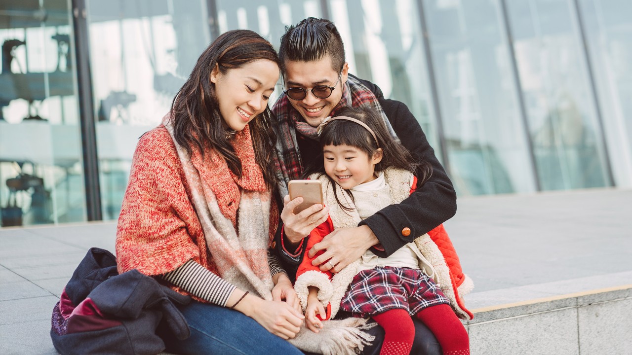 A little girl and her parents are looking at the mobile happily; image used for "protect what matters" 