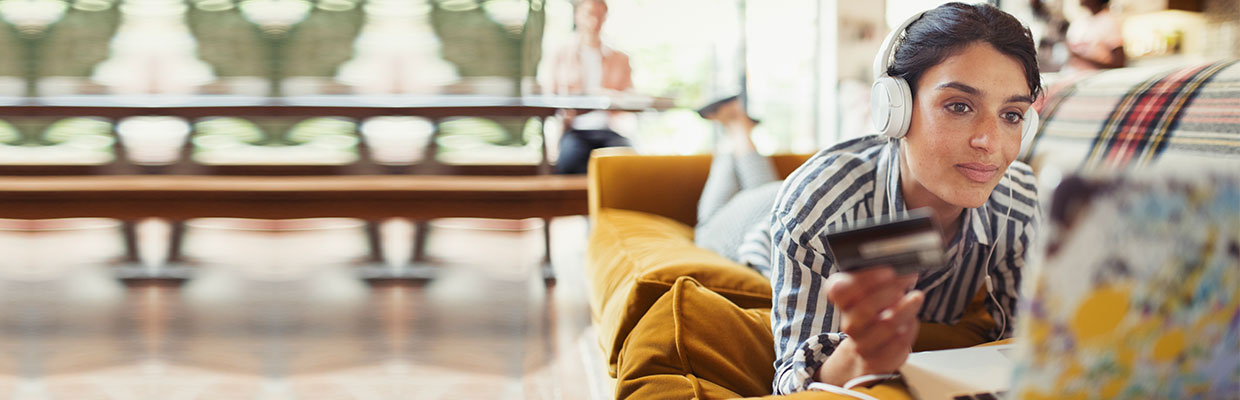 a woman lying on sofa with her credit card and laptop; image used for HSBC LK e-commerce credit cards offers page